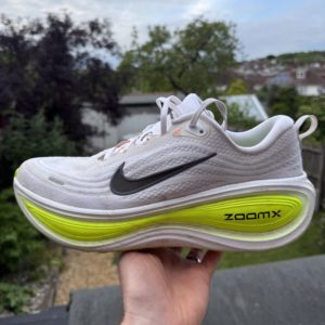 A Nike Vomero Plus right shoe being held in the air by a runner.